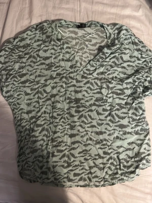 Gråmönstrad blus från Vero Moda - Säljer en luftig blus från Vero Moda i storlek S. Toppen har ett grått zebramönster på ljus bakgrund, v-ringad hals och korta ärmar. Perfekt till jeans eller kjol för en chill look.