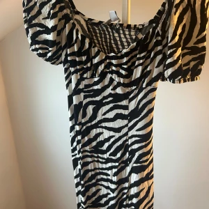Zebramönstrad puffärm klänning - Snygg kort klänning med zebramönster i svart och vitt. Modellen har puffiga korta ärmar och en smickrande, lätt rynkad byst. Perfekt för dig som vill sticka ut med ett djuriskt mönster och cool siluett. Materialet känns lätt och bekvämt mot huden.