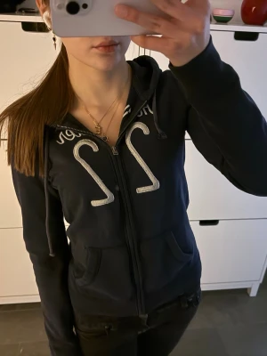 Vintage mörkblå Hollister zip up hoodie  - Vintage mörkblå Hollister huvtröja med dragkedja. Storlek S! I bra skick, förutom en defekt på armen, men jag har bara tvättat den normalt, den borde gå bort med ett starkare tvättmedel! Har den vita Hollister-logotypen över bröstet.
