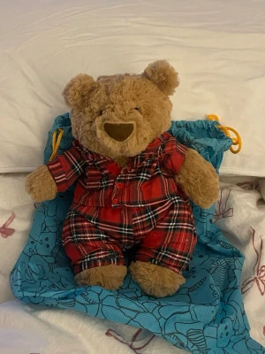 Rutig röd väst från Jellycat - Säljer en superfin röd väst Björn från Jellycat med klassiskt rutigt mönster i svart och vitt. Västen har knappar framtill och är gjord i mjukt bomullstyg. Perfekt för dig som vill addera lite brittisk stil till din outfit.