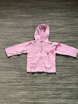 -Ljusrosa hoodie Petit Patapon - Ljusrosa hoodie från Petit Patapon med dragkedja, huva och två små fickor fram. Broderad text 'I ♥ spring' och blommor i rosa på bröstet och ryggen. Stickad känsla och ribbade muddar vid ärmar och nederkant. Perfekt för vårens alla dagar!