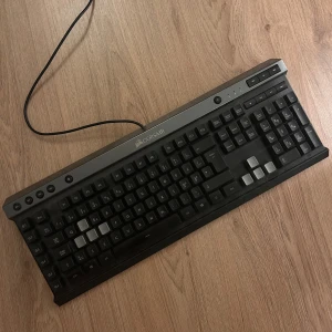 Corsair Gaming Tangentbord (USB, kabelanslutet) - Corsair gaming tangentbord med USB-anslutning. Fullstort med dedikerade makro- och mediaknappar. Något dammigt men i gott skick, alla tangenter syns hela. Perfekt för gaming eller kontor.