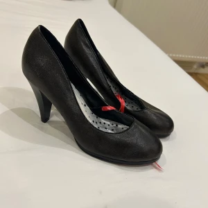 Svarta pumps med klack, stl 38 - Snygga svarta pumps med rund tå och medelklack. Insidan har ett coolt stjärnmönster i svart på silver 