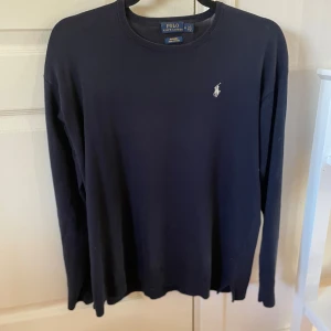 Mörkblå tröja från Polo Ralph Lauren - Snygg mörkblå tröja från Polo Ralph Lauren i mjuk pima bomull. Klassisk rund hals och långärmad modell med den ikoniska broderade loggan på bröstet i vitt. Perfekt för dig som gillar stilrena och tidlösa plagg. Storlek M, men kan även passa S. 