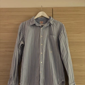 Replay Skjorta - Snygg blå skjorta med vita vertikala ränder från Replay som inte längre används. Långärmad och tillverkad i mjuk bomull som känns skön mot huden. Perfekt för dig som gillar stilrena och fräscha skjortor. Skriv vid frågor eller förslag om pris!