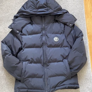 Äkta grå/svart pufferjacka från Trapstar - Äkta Trapstar puffer jacka med logo på framsidan med preset Trapstar stort skriver på bank sidan. Jag säljer den efter som den har blivit liten för mig jackan har alla små detaljer vill ha fler bilder skriv bara till mig för jag kan tyvär ej lägga ut fler bilder på artikeln. Köpte jackan för 1600.PRISET KAN DISKUTERAS!!