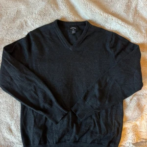 Mörkgrå v-ringad tröja Callaway M - Snygg mörkgrå v-ringad tröja från Callaway i storlek M. Tröjan har långa ärmar och ribbade muddar vid hals, ärmslut och nederkant. Perfekt för dig som gillar stilrena och klassiska plagg med sportig touch.