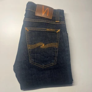 Nudie Jeans  - Mörkblå jeans från Nudie Jeans, modell Tight Long John. Slimmad passform med klassiska orangea sömmar och Nudie-logga på bakfickan. Tillverkade i 98% ekologisk bomull och 2% elastan för extra stretch. Midja 32cm, längd 101cm.  Ifall det inte finns någon bild i annonsen där jag bär plaggen jag säljer så är det för att jag ej kan ha storleken heller passformen, så kolla måtten för storlek och googla på modellnamnet för passform 😉 s3