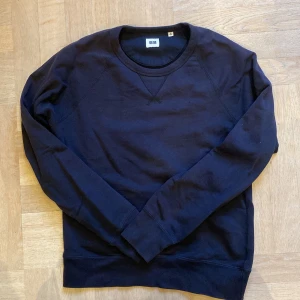 Mörkblå sweatshirt från Uniqlo - En stilren mörkblå sweatshirt från Uniqlo i storlek M. Tröjan har rund hals, ribbade muddar och är tillverkad i mjuk bomull. Perfekt för chill dagar och enkel att matcha med jeans eller joggers. Klassisk passform och långärmad design.