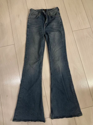 Blå bootcut jeans från Lee - Snygga blå jeans från Lee med klassisk bootcut-passform och femficksdesign. Jeansen har en hög midja och är tillverkade i mjukt denimtyg. Bra skick och väldigt bekväma. Storlek W25 L31