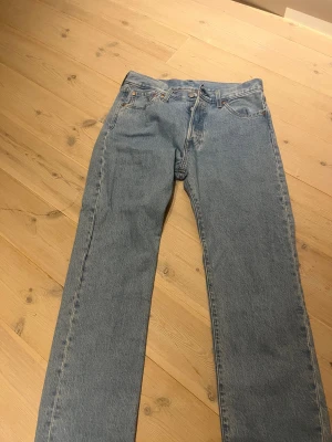 Levi's 501 ljusblå jeans W30 L32 - Klassiska Levi's 501 jeans i ljusblå tvätt med rak passform och fem fickor. Jeansen har knappgylf och är tillverkade i bomull. Perfekt för dig som gillar t stil och vill ha ett par ikoniska jeans i garderoben. Har används 2 gånger så väldigt bra skick. 10/10 skick.