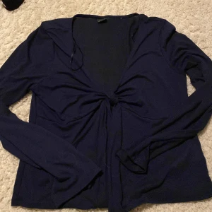 Mörkblå omlottopp med knyt - Snygg mörkblå omlottopp med lång ärm och knyt framtill som ger en cool v-ringad look. Tunn och mjuk i materialet, perfekt för att styla med jeans eller kjol. Enkel men ändå trendig design som passar dig som gillar stilrena plagg.