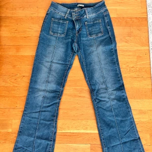 Blå bootcut jeans - Snygga blå jeans med bootcut passform från MadLady Framtill finns två fyrkantiga fickor och markerade sömmar längs benen. Baktill har jeansen klassiska fickor med knappdetaljer. Perfekt för dig som gillar retrovibbar och bekväm stil. Storlek 38-tall men de är uppsydda.MÅTT: Midja(mätt platt): 35 cm Midjehöd fram: 22 cm Innerbens längd: 80 cm Höfter: 43 cm PRIS KAN DISKUTERAS!