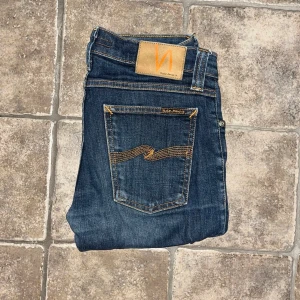 Nudie Jeans  - Snygga mörkblå jeans från Nudie Jeans, modell Tight Long John. De har klassisk femficksdesign, kontrastsömmar och en smal passform med stretch för extra komfort. Materialet är 98% bomull och 2% lycra. Perfekt för dig som gillar en tight och modern look. Midja 36cm, längd 100cm.  Ifall det inte finns någon bild i annonsen där jag bär plaggen jag säljer så är det för att jag ej kan ha storleken heller passformen, så kolla måtten för storlek och googla på modellnamnet för passform 😉 s4