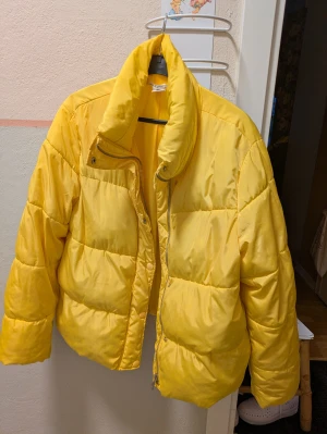 Gul pufferjacka med hög krage Hm  - Säljer en fet gul pufferjacka med hög krage och dragkedja framtill. Jackan har en schysst oversized passform och är quiltad med breda kanaler. Perfekt för dig som vill sticka ut och hålla dig varm under kalla dagar. Jackan har långa ärmar och cool streetstil.Det är storlek 42 men jag är m och ni ser hur den sitter på mig bild 2,3 lite sämre färg kvalitet på självutlösaren så bild ett är precis så 🌞 gul den är 