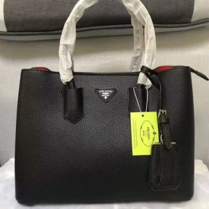 Svart handväska från Prada i skinn - Snygg svart handväska från Prada med klassisk form och struktur i skinn. Insidan är röd och har dragkedja upptill. Väskan har två handtag och en elegant detalj med märkets logga framtill. Perfekt för dig som vill ha en lyxig och stilren accessoar.