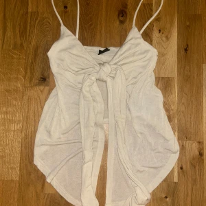 Vit linnetopp med knyt från Gina Tricot - Supersöt vit linnetopp från Gina Tricot med smala axelband och knytning framtill. Sitter snyggt och har en feminin v-ringad form.