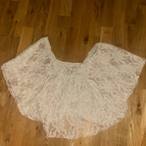 Vit spetsig bolerotopp - Säljer en superfin vit bolerotopp i spets med vid, luftig passform. Toppen är ärmlös och har ett transparent, romantiskt utseende med vackra spetsdetaljer över hela plagget. Perfekt att slänga över ett linne eller ha som den är.