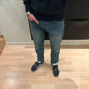 Tiger of Sweden blå jeans straight fit - Tiger of sweden jeans i blå tvätt med rak passform och normal midja. Jeansen har fem fickor, knappgylf och är tillverkade i slitstarkt bomullsjeansmaterial. Perfekta för en chill och tidlös look. Överlag bra skick men som visat på bilderna är de avklippta vid benöppningen 