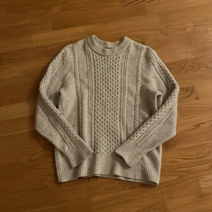 Beige stickad tröja från J.Lindeberg - Säljer en beige stickad tröja från J.Lindeberg i storlek M. Tröjan har ett snyggt flätstickat mönster framtill, ribbade muddar och rund hals. Perfekt för kyliga dagar och riktigt skön att ha på sig. 100% ull