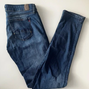 Replay jeans  - Snygga blå jeans från Replay med klassisk femficksdesign och raka ben. Jeansen har en mörk tvätt med lätt slitning och detaljerade sömmar på bakfickan. Märkespatch i läder baktill i midjan. Perfekta för dig som gillar stilrena jeans. W31 L34