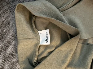 Olive ärmlös tröja Gina Tricot - Snygg beige klänning från Gina Tricot i storlek L. Modellen är ärmlös med en cool krage och omlott-detalj framtill. Materialet känns mjukt och har en lätt struktur, perfekt för dig som gillar stilrena och moderna plagg.