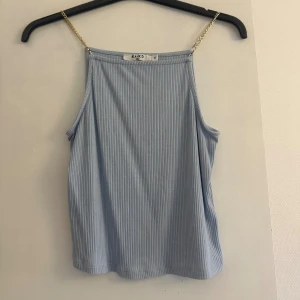 Ljusblå ribbad linnetopp från NA-KD - Supersnygg ljusblå ribbad linnetopp från NA-KD med tunna guldfärgade kedjeband som axelband. Toppen är ärmlös och har en rak, avslappnad passform. Perfekt för varma dagar och enkel att styla med dina favoritjeans eller kjol.