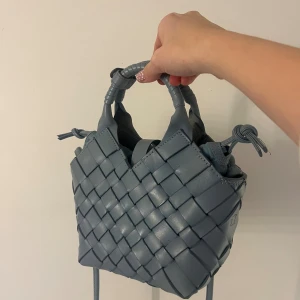 Blå handväska från Cala Jade i skinn - Snygg blå handväska från Cala Jade i flätat skinn med två handtag och justerbar axelrem. Väskan har en unik form och stängs med dragsko i tyg. Perfekt för dig som gillar stilrena detaljer och vill ha något som sticker ut.