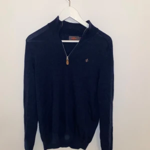 Morris marinblå stickad tröja half zip - Snygg marinblå stickad tröja från Morris med half zip och liten broderad logga på bröstet. Tröjan har lång ärm och ribbade muddar, perfekt för lager-på-lager under höst och vinter.