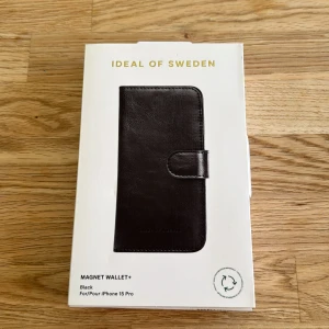 Magnet Wallet+ för iPhone 15 Pro - Snygg och praktisk Magnet Wallet+ i svart från iDeal of Sweden, anpassad för iPhone 15 Pro. Plånboksfodralet har plats för flera kort, magnetstängning och avtagbart skal. Produkten är oanvänd och levereras i originalförpackning.