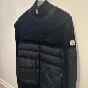 Moncler cardigan  - Svart moncler cardigan,  Jackan har hög krage, dragkedja och Moncler-logga på ärmen. Perfekt för dig som gillar stilren och exklusiv design. Har köpt den på miinto, så den är äkta 