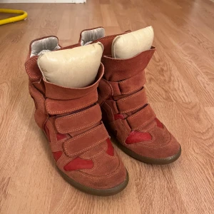 Isabel Marant röda wedge sneakers - Säljer ett par ikoniska Isabel Marant wedge sneakers i röd med coola paneler i skinn. Använda ett fåtal gånger. Unik färg. Inte trasiga eller slitna någonstans, förutom texten inuti skon som är lite bortslipad.