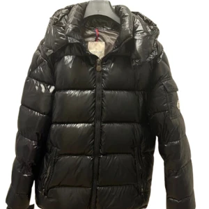 Maya  - Säljer en svart pufferjacka med glansig finish och huva. Jackan har logga på ärmen, dragkedja framtill och praktiska fickor. Insidan har ett unikt serietryck. Perfekt för dig som vill ha en snygg och varm vinterjacka med streetkänsla.