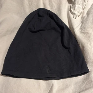 Svart mössa Peak Performance - Svart mössa från Peak Performance i stilren design med diskret broderad logga framtill. Tillverkad i mjuk bomull som sitter skönt på huvudet. Perfekt för dig som gillar enkel och clean stil. strl s/m