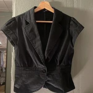 Figursydd kavaj - Svart väst/kavaj från H&M med kort passform.  Västen har en knapp framtill och markerad midja med sömmar. Sparsamt använd och extra knapp finns. 
