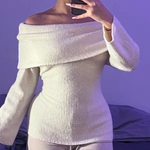 Offshoulder ribbad stickad tröja - Säljer en ljus, ribbad stickad tröja med offshoulder-design och lång ärm. Tröjan har en bred krage som vilar snyggt över axlarna och ger en trendig look. Perfekt för dig som gillar stilrena och bekväma plagg med lite edge.