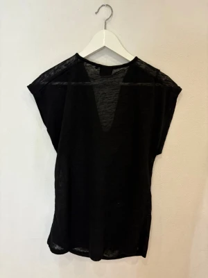 Svart transparent blus från bunon P - Säljer en svart, tunn och transparent blus från Bunon P. Toppen har en snygg draperad halsringning och är ärmlös med loose passform. Perfekt för dig som gillar en stilren look med lite edge. Materialet känns lätt och luftigt mot huden.