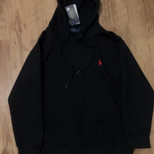 Svart hoodie från Polo Ralph Lauren - Svart hoodie från Polo Ralph Lauren med klassisk röd broderad logga på bröstet. Tröjan har huva med snörning och långa ärmar. Mjuk bomullskvalitet som är skön att bära och passar perfekt till chill dagar. En stilren och enkel look som alltid funkar.                 helt Ny oanvänd priset kan diskuteras 