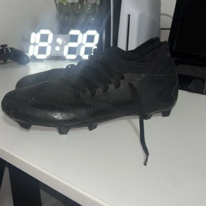 Adidas predator  - Säljer ett par helsvarta fotbollsskor från Adidas med klassisk design och snörning. Skorna har låg profil, rund tå och platt sula med dobbar för bra grepp på planen. Tillverkade i syntetmaterial för lätt känsla och smidig passform. Perfekta för dig som vill ha stilrena skor på matchen.