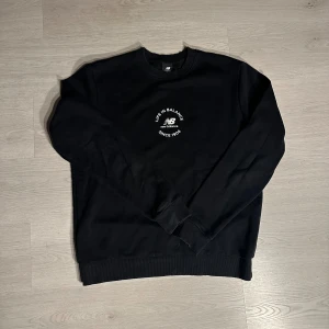 Svart New Balance - Svart sweatshirt från New Balance med vitt broderat tryck på bröstet där det står 'Life in Balance Since 1906'. Tröjan har rund hals, ribbade muddar vid ärmslut och nederkant samt lång ärm. Perfekt för en chill och sportig look.