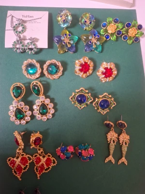 Färgglada statement örhängen, mix vintage  - Säljer ett gäng unika och färgglada statement örhängen i olika former och färger. Här finns blommiga örhängen i blått, grönt och gult, röda hjärtformade örhängen med guld, blå och gröna stenar, samt coola sjöjungfruörhängen i guld. Perfekt för dig som vill sticka ut och älskar färg!