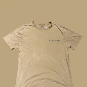 Beige t-shirt från Polo Ralph Lauren - Snygg beige t-shirt från Polo Ralph Lauren med diskret logga på bröstet. Klassisk rund hals och korta ärmar. Tillverkad i mjuk bomull som känns skön mot huden. Perfekt för en chill och stilren look.