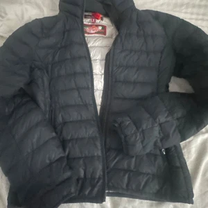 Svart dunjacka från Parajumpers - Säljer en svart dunjacka från Parajumpers i storlek S. Jackan är quiltad med dragkedja framtill och har en ljusgrå insida. Den är lättviktig och har en hög krage, perfekt för kyliga dagar. Snygg och stilren design som funkar till många olika outfits.