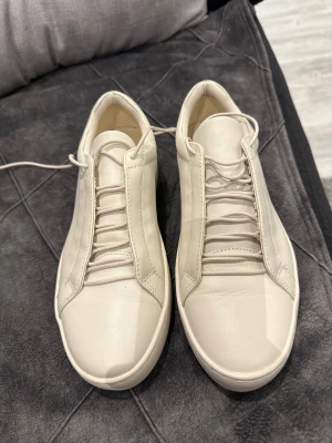 Vita sneakers från Vagabond - Säljer ett par stilrena vita sneakers från Vagabond med rund tå och platt sula. Skorna har snörning och är tillverkade i mjukt skinn med diskreta sömmar och minimalistisk design. Perfekta för dig som gillar cleana och klassiska sneakers.