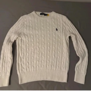 Vit stickadtröja från Polo Ralph Lauren - Vit  stickad tröja från Polo Ralph Lauren med klassisk broderad logga på bröstet. Tröjan har lång ärm och rund hals, perfekt för lager-på-lager. Snygg och tidlös design som funkar året runt.