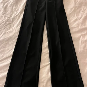 Svarta kostymbyxor  - Snygga svarta kostymbyxor med rak och vid passform. Byxorna har pressveck framtill och är tillverkade i ett slätt tyg som ger en clean look. Perfekta för dig som gillar stilrena och klassiska vibes. Priset går att diskutera!