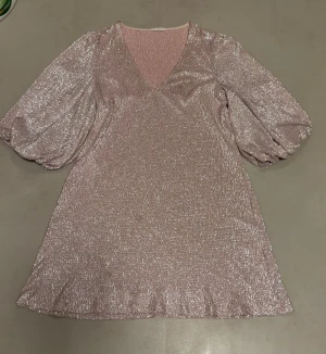 Glittrig rosa kortklänning Ida Sjöstedt - Superfin glittrig rosa klänning från Ida Sjöstedt med v-ringning och puffiga långärmar. Kort modell med skimrande material som verkligen sticker ut. Perfekt för dig som vill ha något extra och älskar glitter. Snygg passform och mjukt tyg.