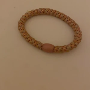 Beige flätat armband med detalj - Snyggt armband i beige med flätad design och en rund detalj i mitten. Armbandet har en enkel och stilren look som passar till många olika outfits. Perfekt accessoar för dig som gillar en naturlig och avslappnad stil.