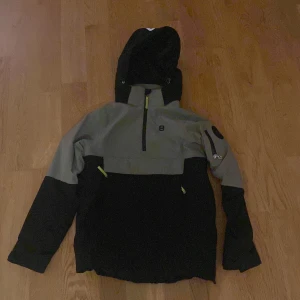 Svart och beige skidjacka 8848 Altitude - Snygg skidjacka från 8848 Altitude i svart och beige med huva och halv dragkedja framtill. Jackan har coola detaljer som fickor med dragkedja och logga på ärmen. Perfekt för dig som gillar skidåkning.