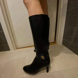 Svarta stövlar från Ralph Lauren - Eleganta svarta stövlar i skinn från Ralph Lauren med klack och guldfärgad RLL-logga. Stövlarna har en dragkedja på insidan för enkel på- och avtagning. Stövlarna är i storlek 36/37 och helt oanvända då de är lite för små för mig. 